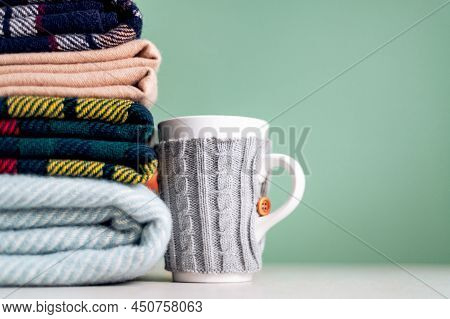 Stack Of Folded Woolen Checked Blankets And Mug In Wollen Cover, Autumn And Winter Concept