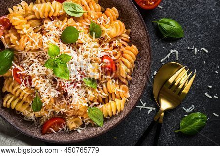 Italian Pasta Alla Arrabiata With Basil And Parmesan On Dark Table. Fusilli Pasta With Tomato Sauce.