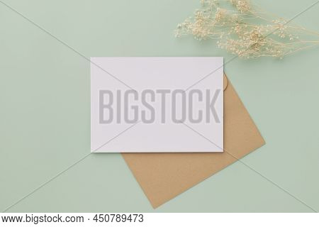Blank Greeting Card Invitation Mockup 5x7 On Brown Envelope With Dried Flowers On Pastel Green Backg
