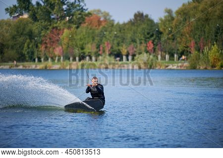 Wakeboarder Surfing On Lake. Young Man Surfer Having Fun Wakeboarding In The Cable Park. Water Sport