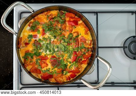 Scrambled Eggs With Vegetables And Herbs In Black Frying Pan On White Stove. Top View