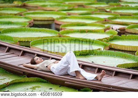 Asian Girl Is Lying Down On The New Vintage Wood Boat On The Lily Lotus Leaf Pond At Outdoor Field.