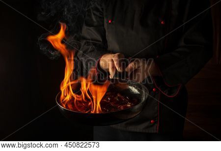 Chef Prepares Vegetable Food In A Frying Pan With A Flame Of Fire. The Concept Of Restaurant And Hot