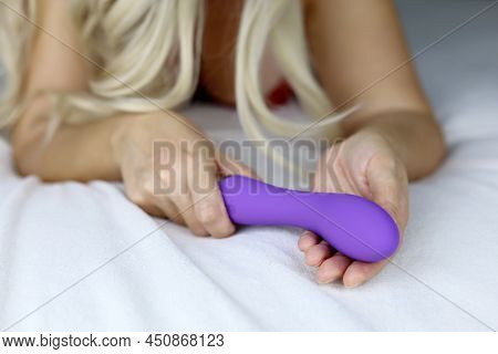 Woman With Vibrator In Hand, Selective Focus. Blonde Girl Laying On A Bed With Dildo, Sex Toy For Ad