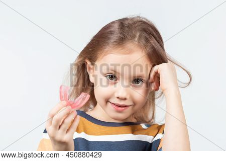 Cute Little Caucasian Girl With Blond Hair Is Holding A Pink Dental Myofunctional Trainer On White T