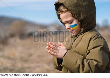 Ukrainian Boy Closed Her Eyes And Praying To Stop The War In Ukraine. Hands Folded In Prayer Concept