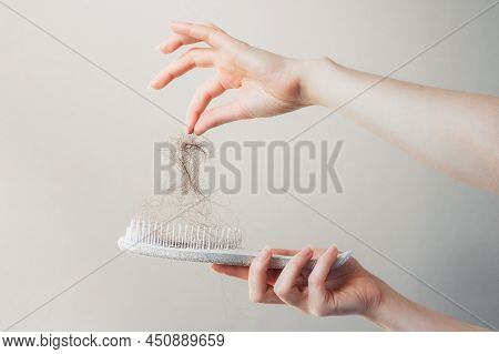 Close-up Of Female Hands Pulling Out Fallen Hair From A Comb. Gray Background. The Concept Of Hair L