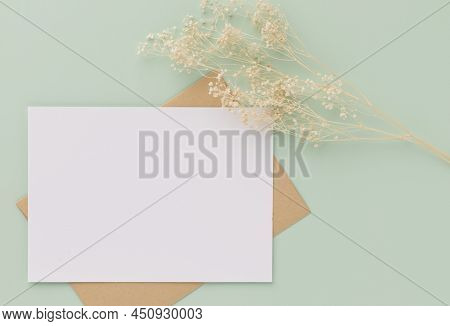 Blank Greeting Card Invitation Mockup 5x7 On Brown Envelope With Dried Flowers On Pastel Green Backg