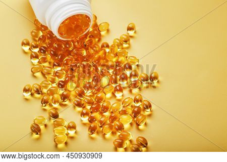 Gold Vitamin D3 Capsules Poured Out Of A Jar On A Yellow Background With Free Space