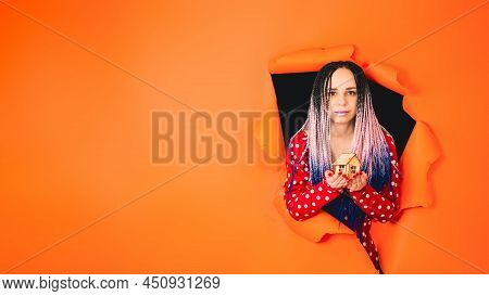 Woman With Toy House Looking Through Hole In Paper. Female With Afro Braids And Miniature Wooden Hou