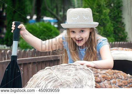 Cheerful Girl Preschooler In The Amusement Park Floats On A Boat On The Water And Enjoys This Little