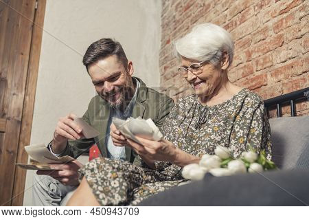 European Businessman In His 30s And His Retired Vivacious Mother Cheerfully Looking At Old Photograp