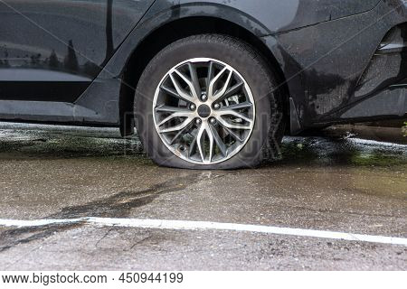 A Passenger Car With A Flat Tire Stands On The Pavement, Wet From The Rain, Waiting For A Service Ca
