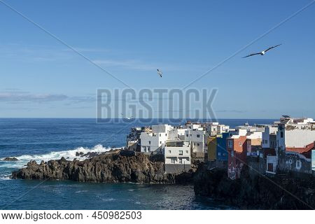 View On Colorful Houses And Black Lava Rocks In Small Village Punta Brava Near Puerto De La Cruz, Te