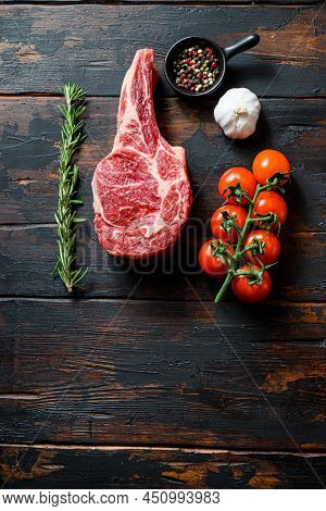 Raw Uncooked Black Angus Beef Ribeye Steak, Bone-incloseup With Tomatoes Garlic Herbs And Peppercorn