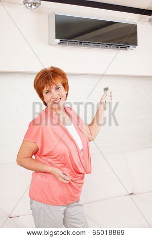 Woman holding a remote control air conditioner at home. Happy mature woman on sofa