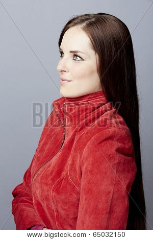 Portrait of a young business woman on gray studio background, wearing red suede leather jacket with long brunette hair