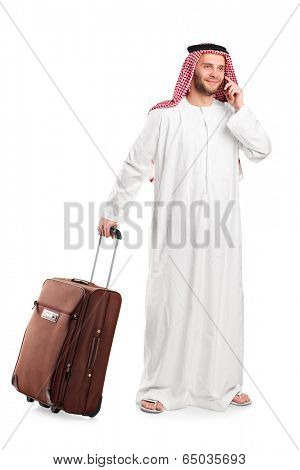 Full length portrait of an Arabic sheik talking on phone and carrying a luggage isolated on white background