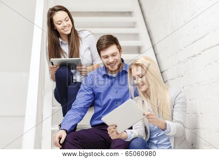 business, technology and startup concept - smiling creative team with tablet pc computer sitting on staircase