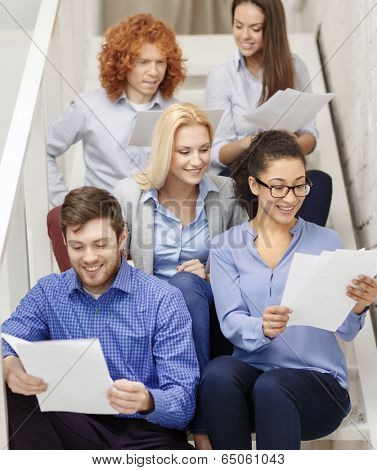 business, office and startup concept - smiling creative team with papers and take away coffee on staircase