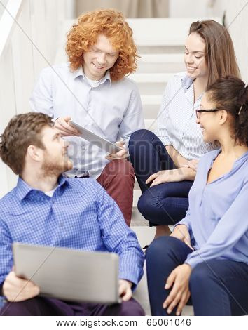 business, technology and startup concept - smiling creative team with laptop and tablet pc computer sitting on staircase