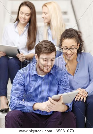 business, technology and startup concept - smiling creative team with tablet pc computer sitting on staircase
