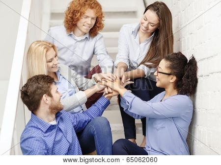 business, office, gesture and startup concept - smiling creative team with hands on top of each other sitting on staircase