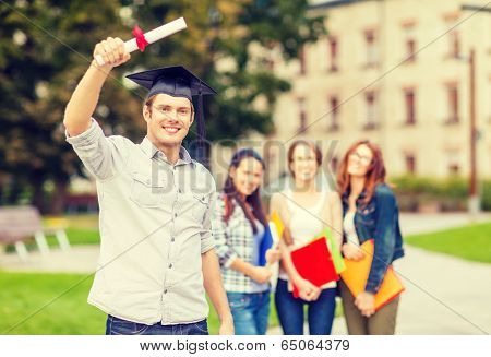 education, campus and teenage concept - smiling teenage boy in corner-cap with diploma and classmates on the back
