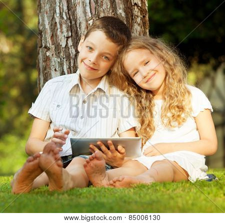 Children with tablet computer outdoors. Girl and boy playing at pc 