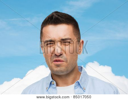 emotions, facial expression and people concept - man wrying of unpleasant smell over blue sky and cloud background