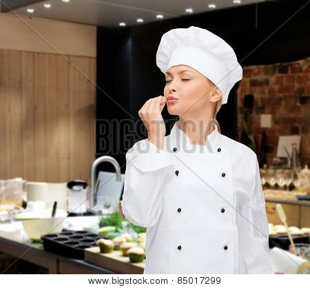 cooking, bakery, gesture and food concept - smiling female chef showing delicious gesture over restaurant kitchen background