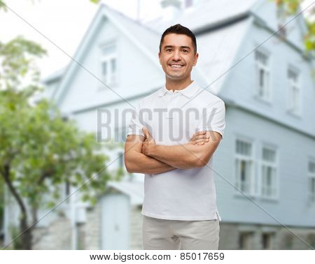 happiness and people concept - smiling man in white t-shirt with crossed arms over house background