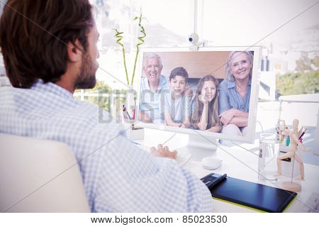 Desinger working on his computer against portrait of grandparents and two kids in living room