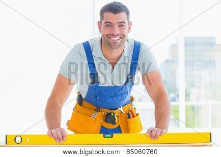 Portrait of smiling handyman using spirit level in bright office
