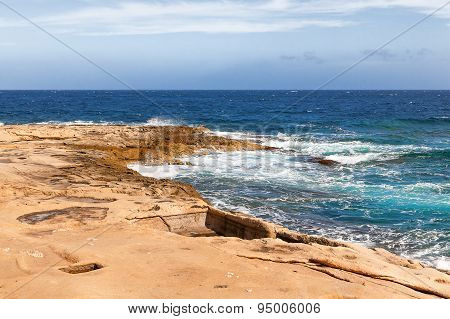 The Waves Beat Against The Rocky Shore. Water Flooded Depressions In The Rocks. Malta, Saint Julians
