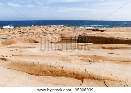 The Waves Beat Against The Rocky Shore. Water Flooded Depressions In The Rocks. Malta, Saint Julians