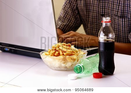 Bottles of softdrinks or soda, chips and man working on a laptop computer in the background