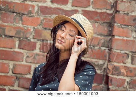 Woman dreaming - portrait of happy lovely and beautiful mixed race Asian Caucasian young woman with closed eyes outdoor against brick wall background. Student or school girl retro style