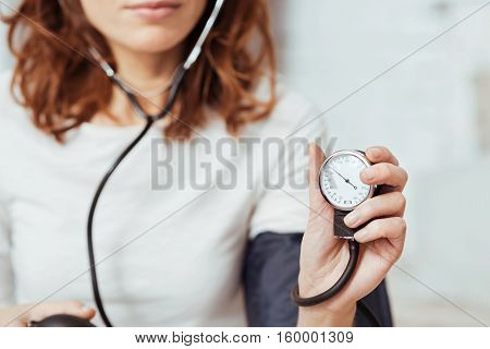 Lead healthy lifestyle. Pleasant concentrated woman hlding tonometer and measuring blood pressure