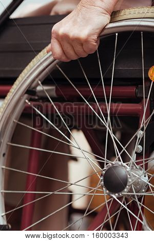 I need it. Close up of wheel of the wheel chair with pleasant elderly woman using it