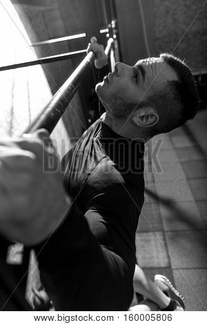 Pull up exercises. Serious well built handsome man holding a horizontal bar and doing pull ups while having an intensive workout