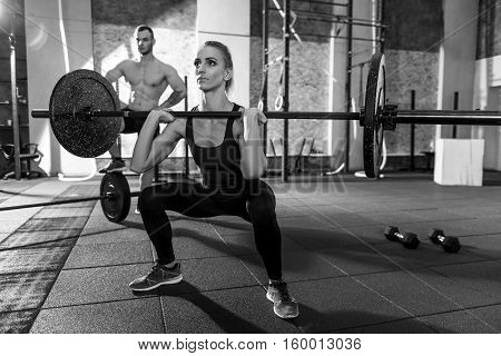 Powerlifting training. Strong well built beautiful woman squatting and holding a barbell while lifting it