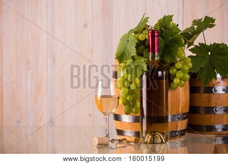 Bottle of white wine with barrels grapes and grapeleaves on glass
