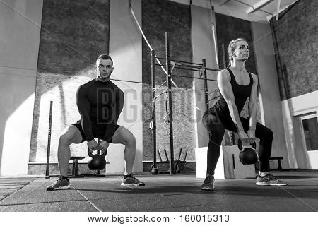 Working out together. Strong good looking well built man and woman holding kettlebells and lifting them while moving synchronically