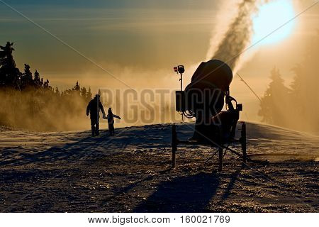 Father is playing with his children next to the snow cannon.