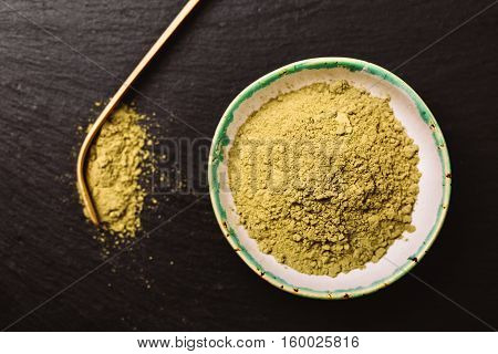 Spoon for matcha tea and green pouder in special ceramics sauser. Black background. Photo made in flat lay style. Focus is on matcha pouder.