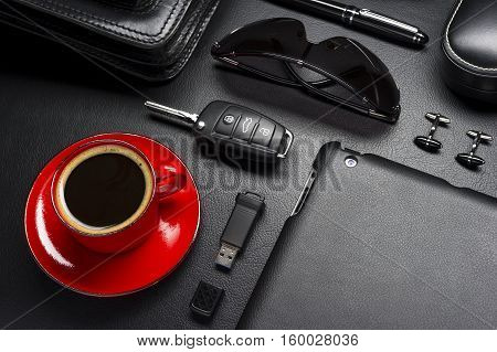 Man accessories in business style with cup of coffee, gadgets, car key, cufflinks, eyewear, briefcase and other luxury businessman attributes on leather black background, fashion industry, selective focus
