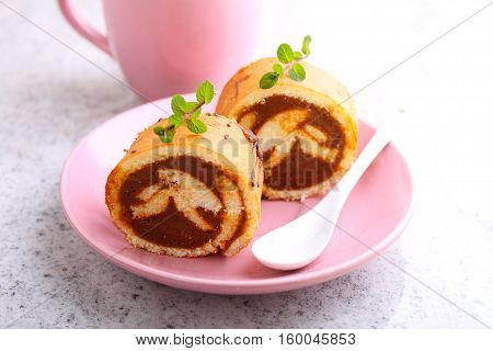 Swiss roll with condensed milk in a pink plate decorated with mint