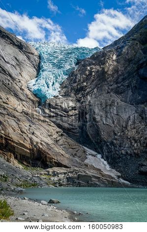Vertical photo with close view of Briksdalsbreen glacier and melted ice lake, turquoise ancient ice in the rocky mountains. Briksdal, Norway.