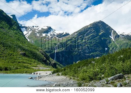 Melted ice lake landscape and group of tourists. Popular hiking path to Briksdalsbreen glacier. Norway.